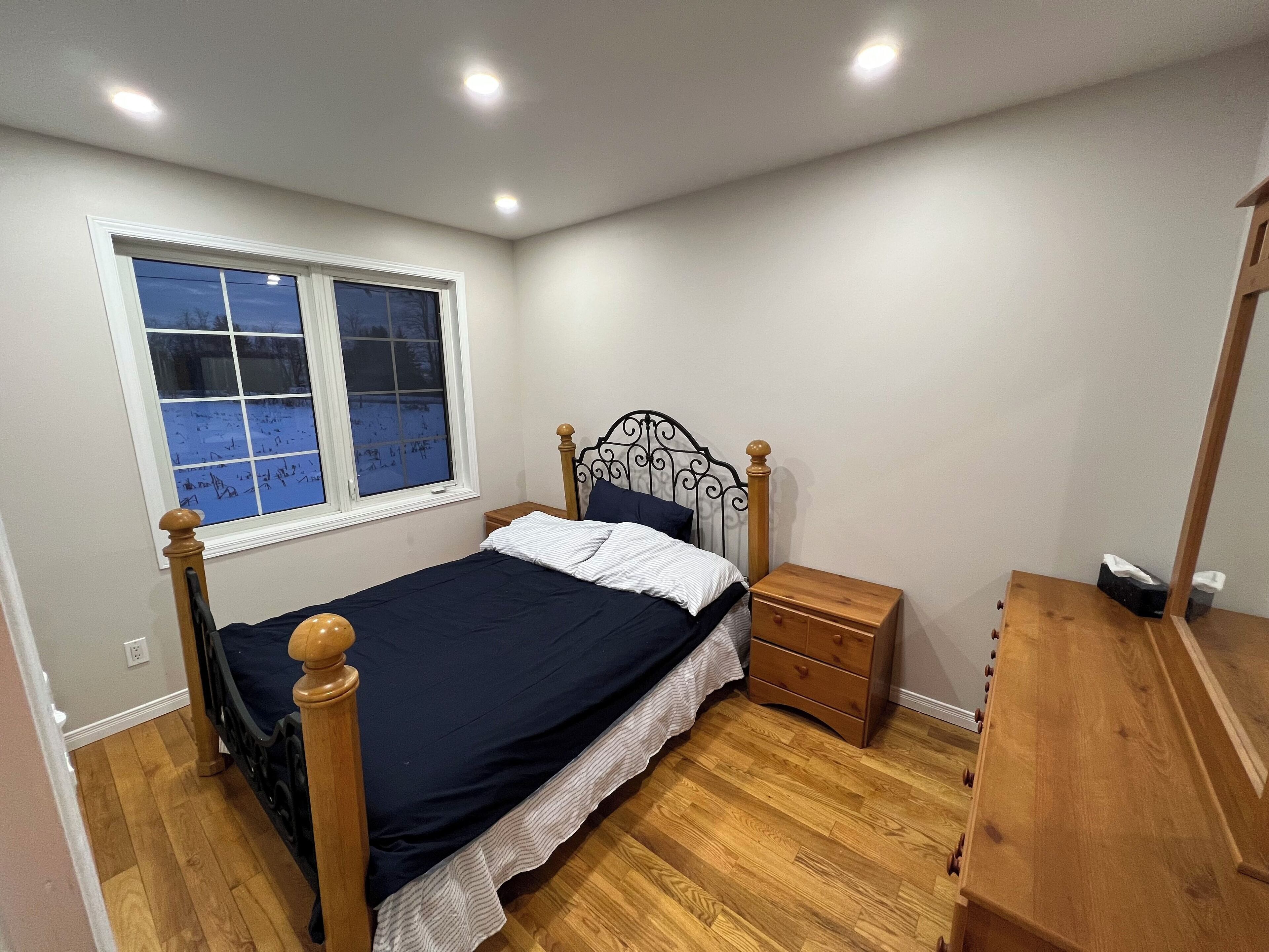 Un dormitorio con cama, mesita de noche, cómoda y ventana con vistas a un paisaje nevado.