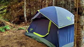 A Coleman tent set up in a forested area.