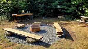A rustic outdoor setting with picnic tables, a grill, and metal cups on a wooden table. - Chickadee Hollow: Rustic Eco Camping near Acadia National Park! (Surry)