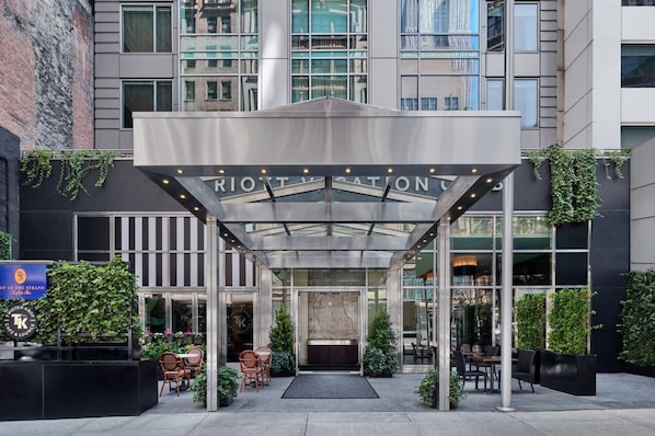 A hotel entrance with a covered patio area, outdoor seating, and a map mural on the wall.