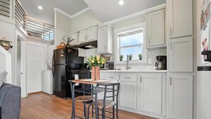 Una cocina moderna con armarios blancos, un refrigerador negro, una zona de comedor con dos sillas y una pequeña mesa.