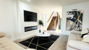 A modern living room with a flat-screen TV, a fireplace, a staircase, and a large abstract painting.