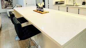 A modern kitchen with a large island, bar stools, a pendant light, and a backsplash.