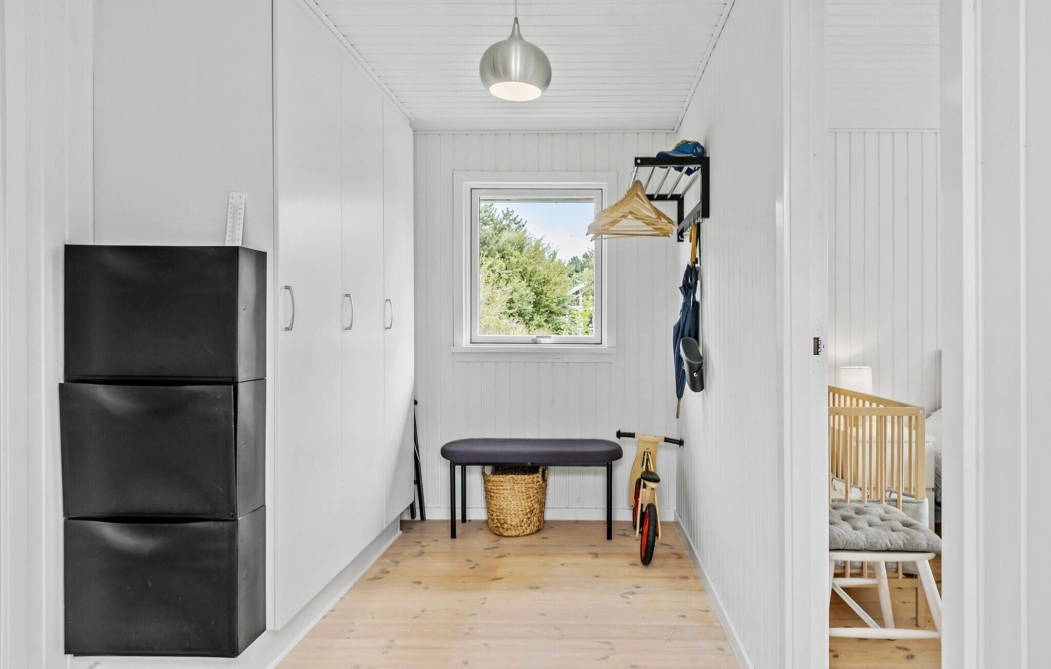 A narrow hallway with a black refrigerator, a bench, a bicycle, and a crib.