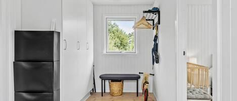 A narrow hallway with a black refrigerator, a bench, a bicycle, and a crib.