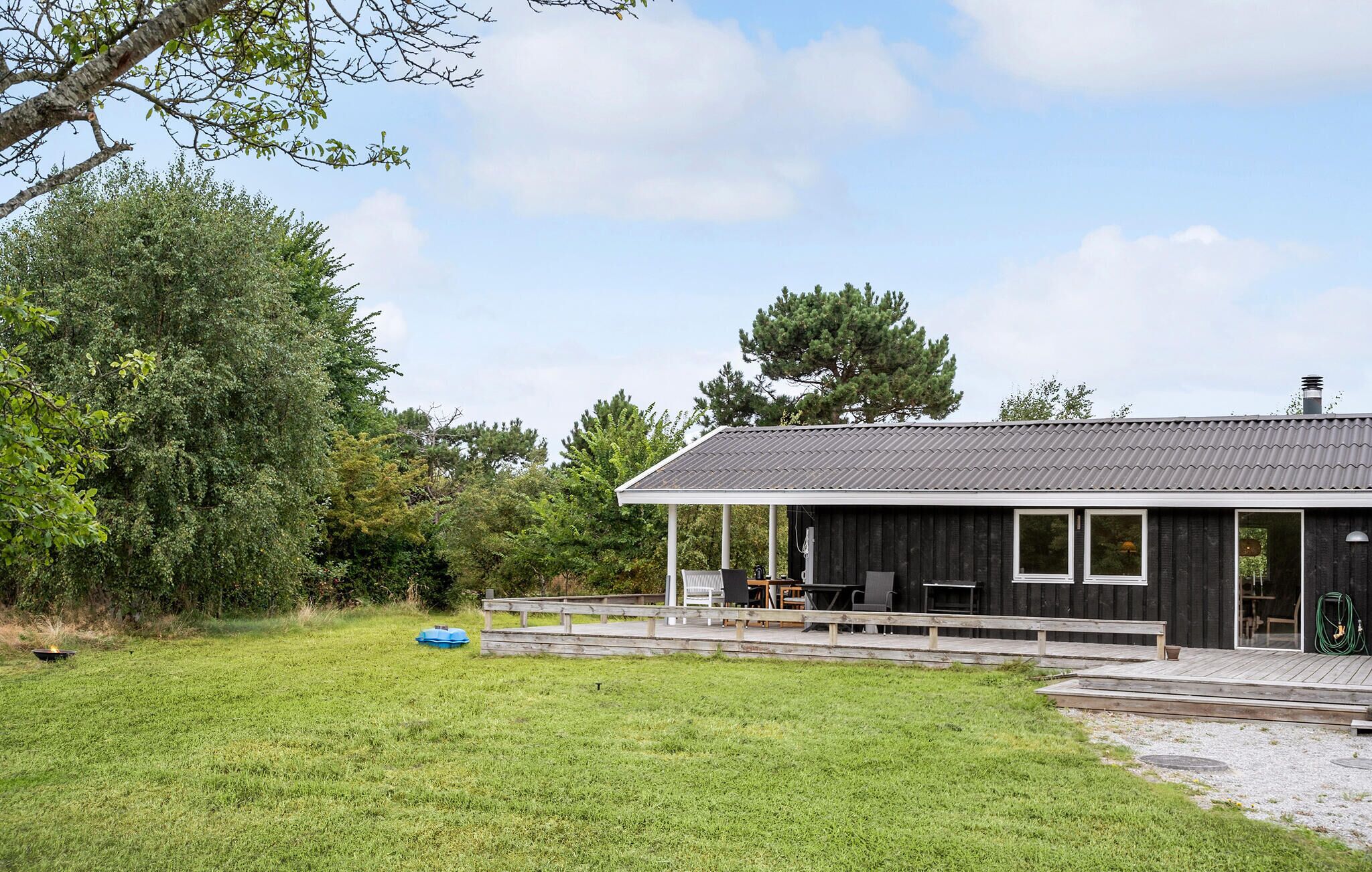 Une cabane moderne dotée d’un porche couvert, d’une petite terrasse et d’une cour gazonnée.
