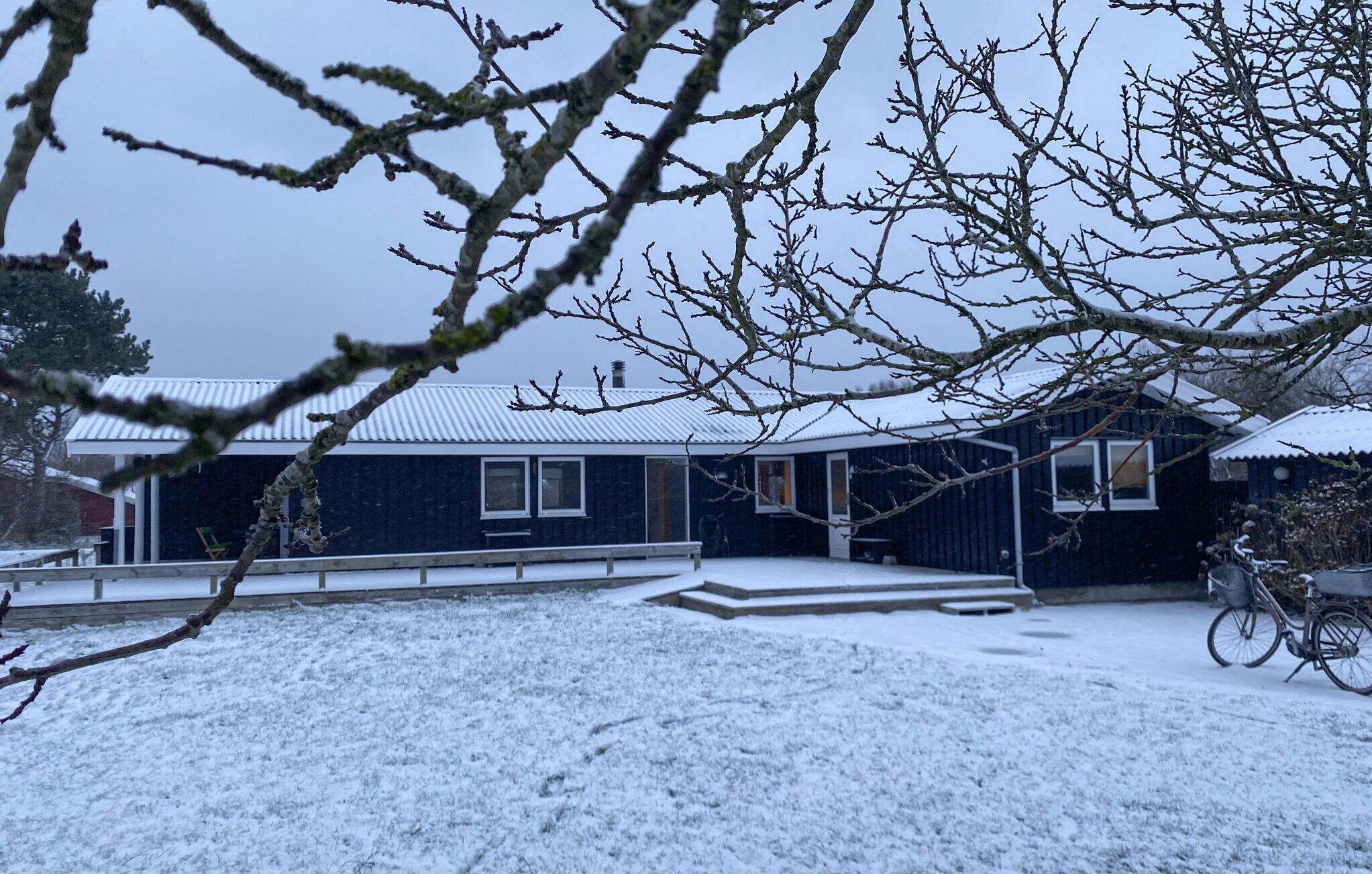 A snow-covered house with a porch and a bicycle.
