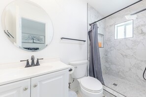 Un baño con un lavamanos blanco, un inodoro, una ducha con puerta de cristal y una pared con azulejos de mármol.