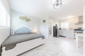 Un dormitorio con cama, mesita de noche, lámpara de pared y baño visible a través de una puerta abierta.