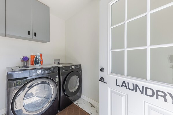 Un cuarto de lavandería con dos lavadoras Samsung, un armario arriba y una puerta con la inscripción 'LAUNDRY'.
