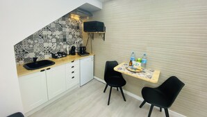 A compact kitchen with white cabinets, a coffee machine, and a small table with chairs.