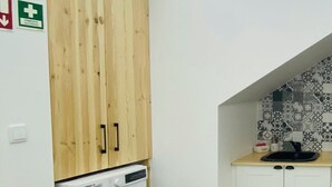A laundry room with a washing machine, a fire extinguisher, and a trash bin.