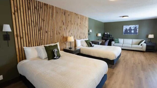 Habitación de hotel con dos camas, cabecero de madera, sofá y televisor montado en la pared.
