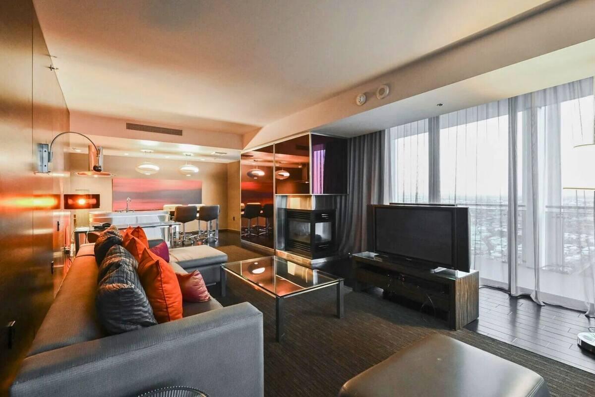 Een moderne hotelkamer met een zithoek, een flatscreen televisie, een eettafel en een groot raam met uitzicht op de stad.