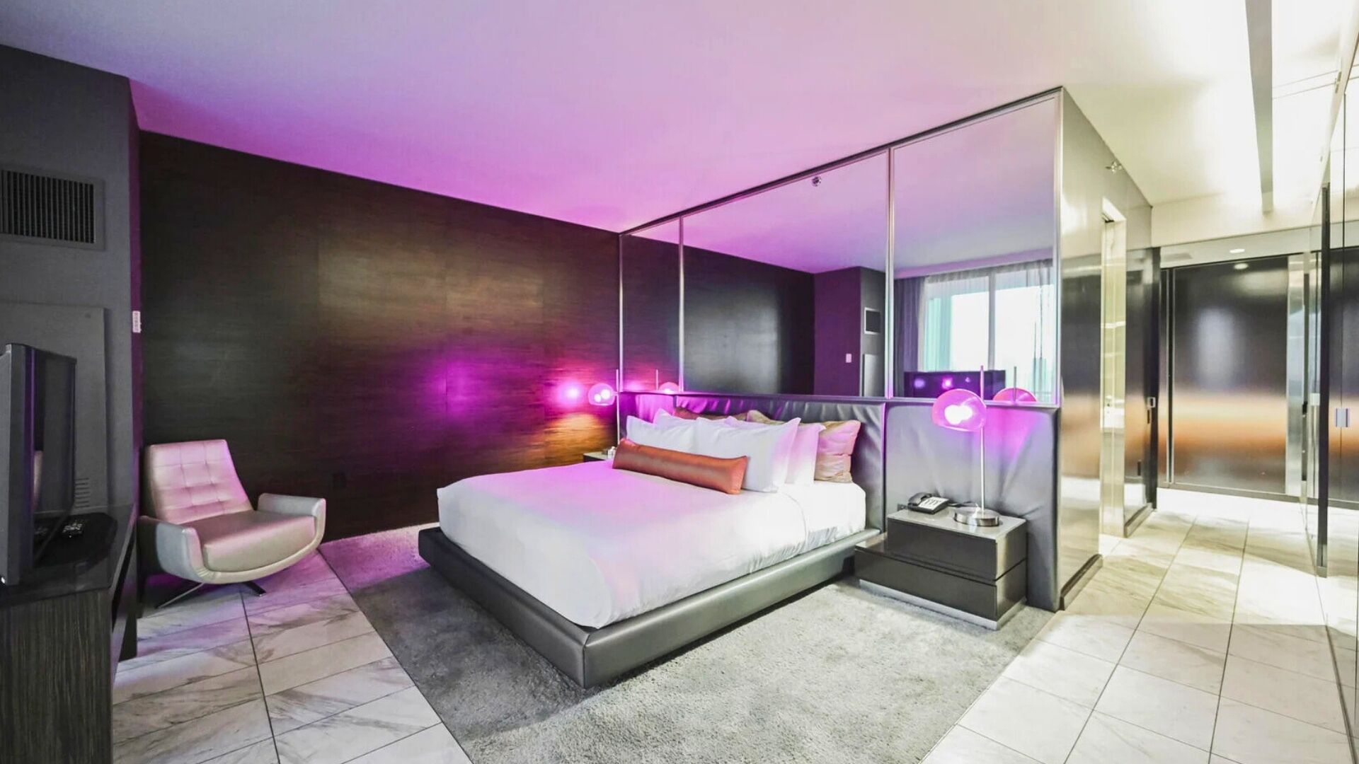 Une chambre à coucher moderne avec un grand lit, une chaise, une table de chevet avec une lampe et un grand miroir.