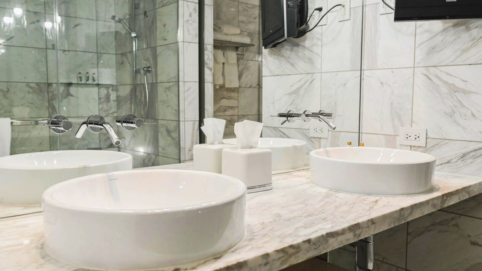 Une salle de bain moderne avec trois lavabos blancs, une douche en verre et un grand miroir.