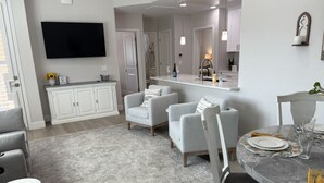 A modern kitchen with a flat-screen TV, white cabinets, and a dining area with a marble table and chairs. - River Trail Stays - Rivers Edge (Tucson)