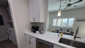 A modern kitchen with white cabinetry, a dishwasher, a coffee maker, and a sink. - River Trail Stays - Rivers Edge (Tucson)