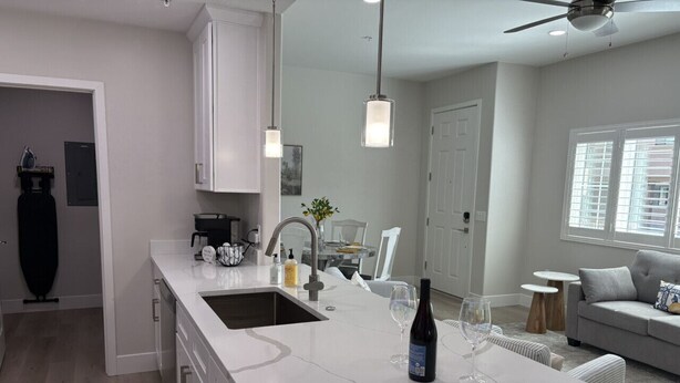 A modern kitchen with a large island, a dining area with a glass table, and a living room with a grey sofa. - River Trail Stays - Rivers Edge (Tucson)