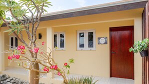 A building with a yellow facade, a red door, and a small tree with pink flowers in the foreground.