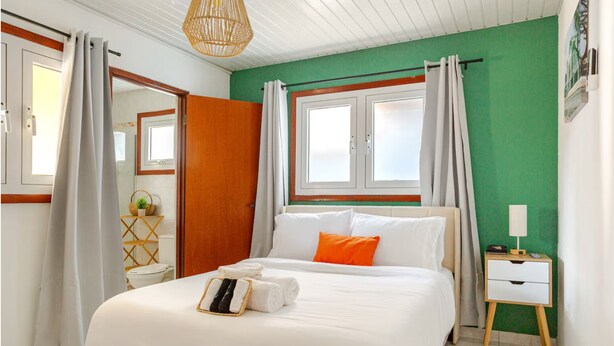 A hotel room with a bed, a bedside table with a lamp, a mirror, and a window with curtains.