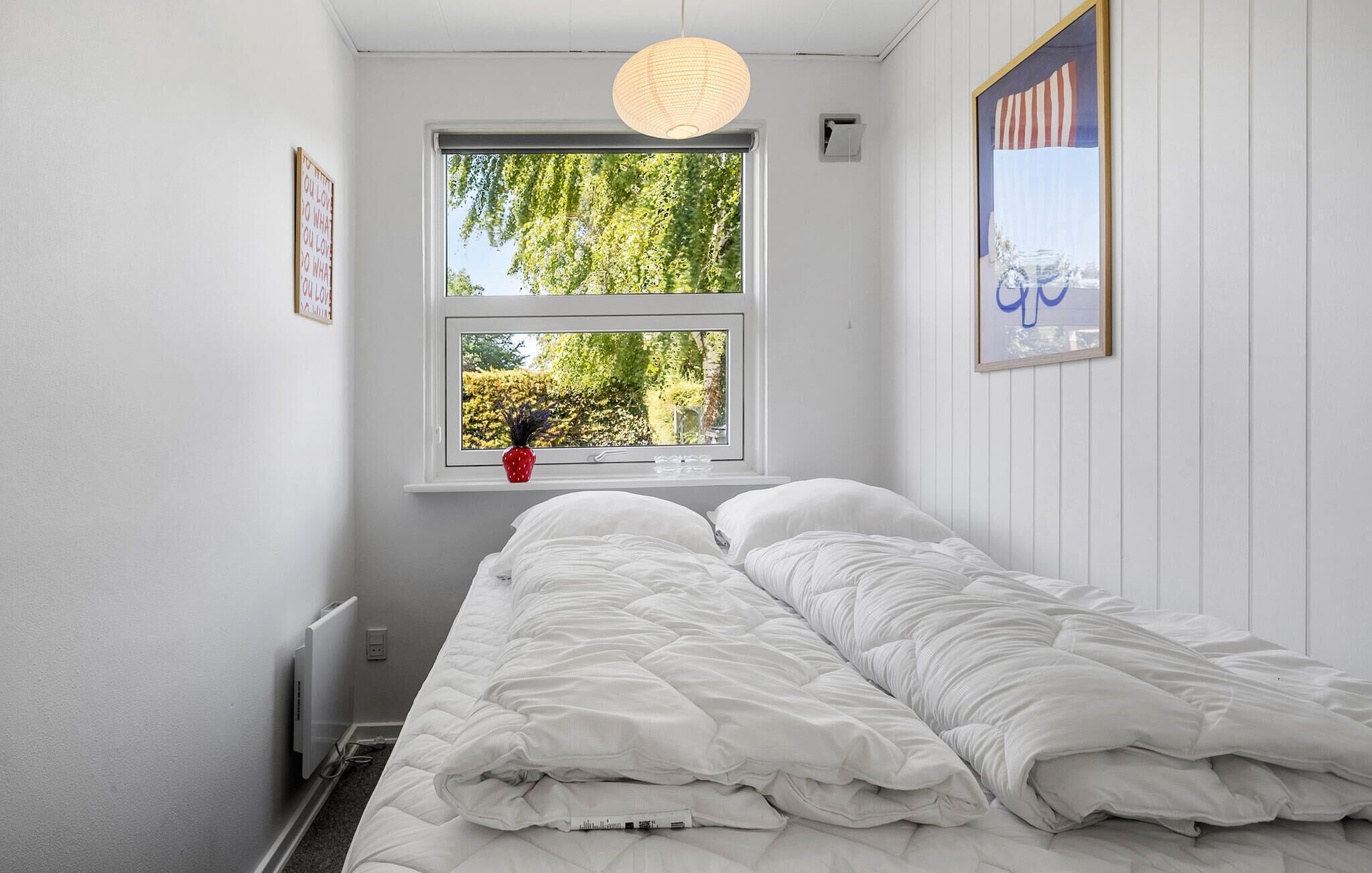A bedroom with a bed, a window with a view of trees, and a wall-mounted radiator.
