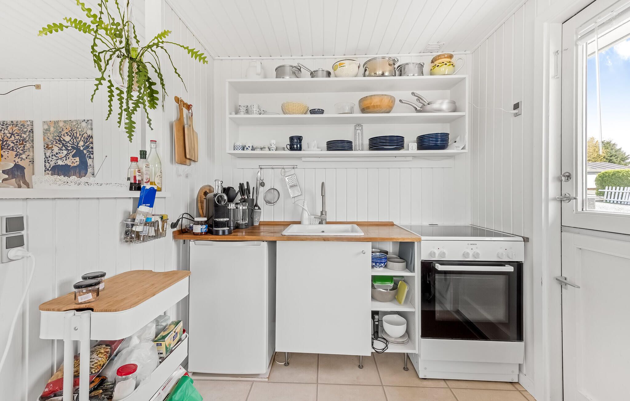 Een compacte keuken met witte kastjes, een Bosch oven en diverse keukengerei op planken.