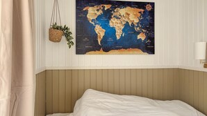 A bedroom with a bed, a world map on the wall, a hanging plant, and a bedside lamp.