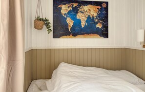 A bedroom with a bed, a world map on the wall, a hanging plant, and a bedside lamp.