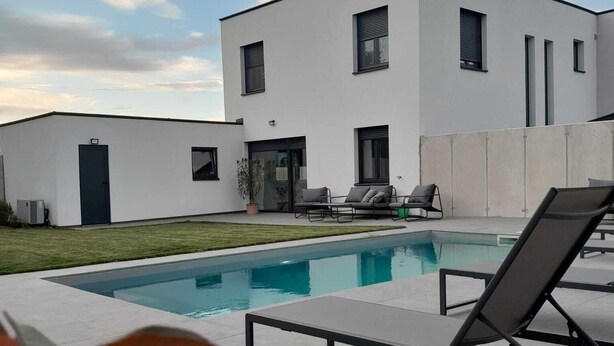 Una casa moderna de dos pisos amb piscina, zona d'estar a l'aire lliure i un jardí ben cuidat.