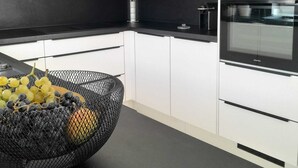 Una cuina moderna amb armaris blancs, taulells negres i electrodomèstics d'acer inoxidable.