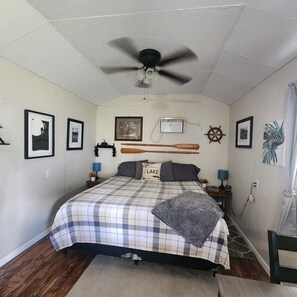 Un dormitorio con una cama, ventilador de techo, obras de arte enmarcadas y un adorno de timón de barco.