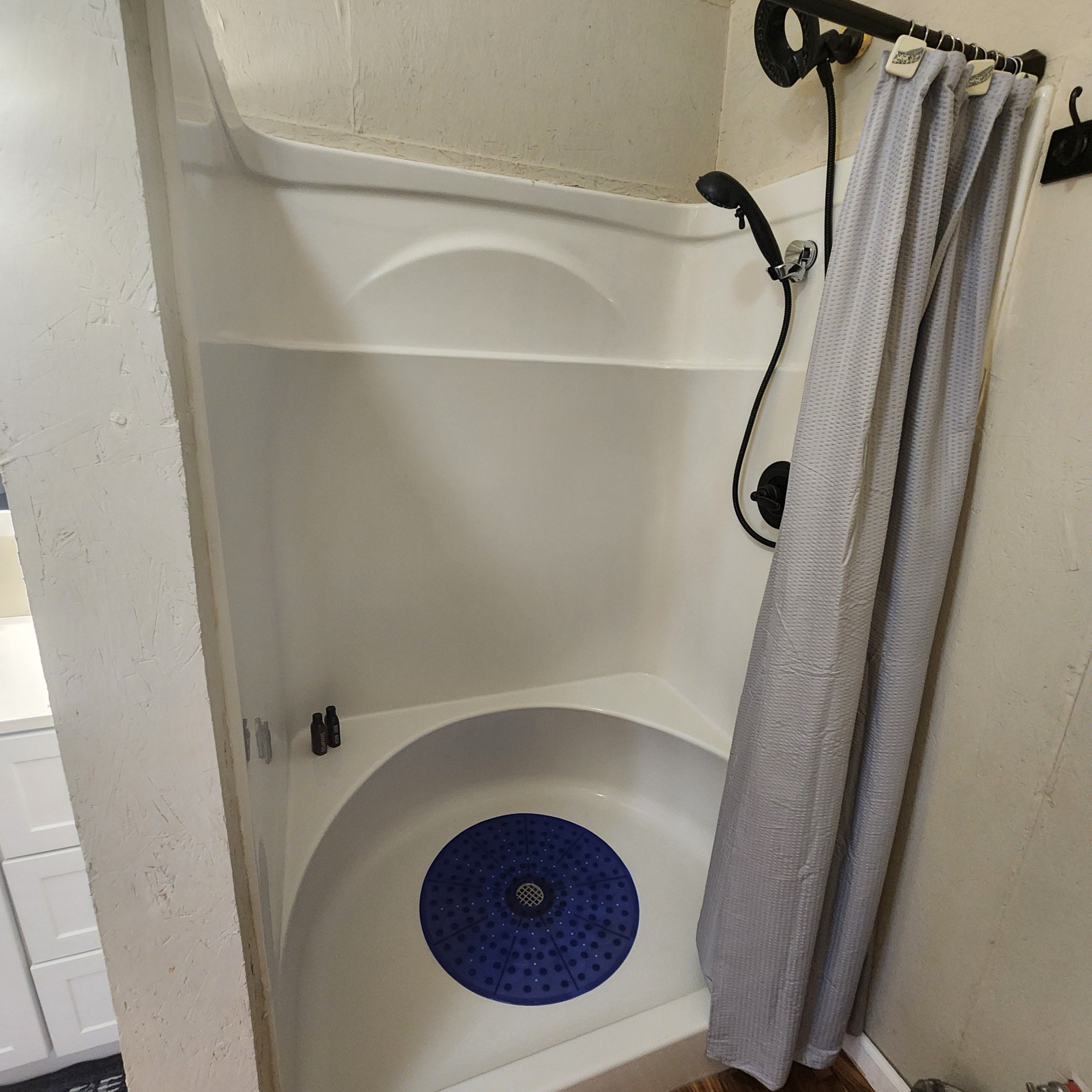 Une douche avec un drain circulaire bleu, une baignoire blanche et un rideau de douche.