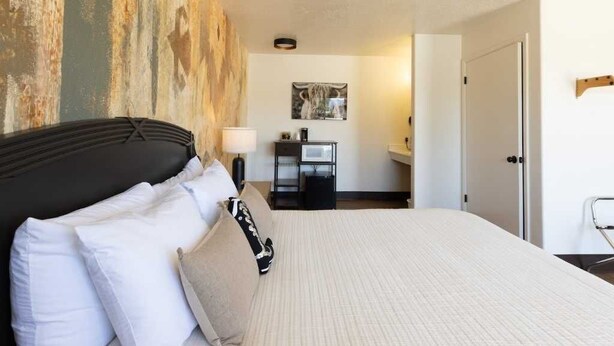 Una cama bien tendida con almohadas blancas y beige, un cabecero y una pared con textura.