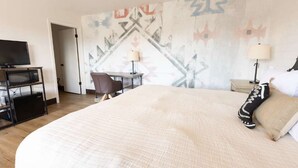 Una habitación de hotel con una cama grande, un escritorio, una silla, un televisor y una pared con un diseño geométrico.