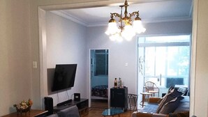 Una sala de estar moderna con una gran mesa de comedor, asientos de cuero azul, un televisor y una araña.