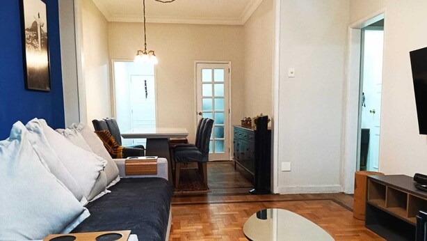 Una sala de estar con un sofá, una mesa de centro, una zona de comedor con una mesa y sillas, y un televisor en la pared.