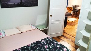 Un dormitorio con una cama, una puerta que da a una sala de estar y un cuadro con una vista urbana.