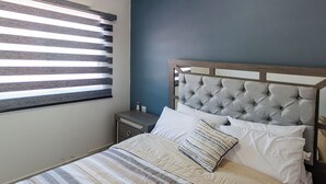 A bedroom with a striped bedspread, a tufted headboard, and a nightstand with a lamp. - Flamingos 45 - Vacation Home for rent 5 min from Ixtapa's hotel zone! (Ixtapa-Zihuatanejo)