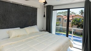 A bedroom with a large bed, a dark textured wall, and a view of a swimming pool and buildings through a glass door. - Flamingos 45 - Vacation Home for rent 5 min from Ixtapa's hotel zone! (Ixtapa-Zihuatanejo)