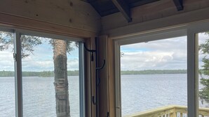 A wooden cabin with a view of a lake, a deck, and a trash can with towels.