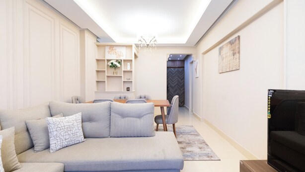 A modern living room with a sofa, TV, and dining area. - 2BRs CityStar Mall Apartment (Al Golf, Nasr City)