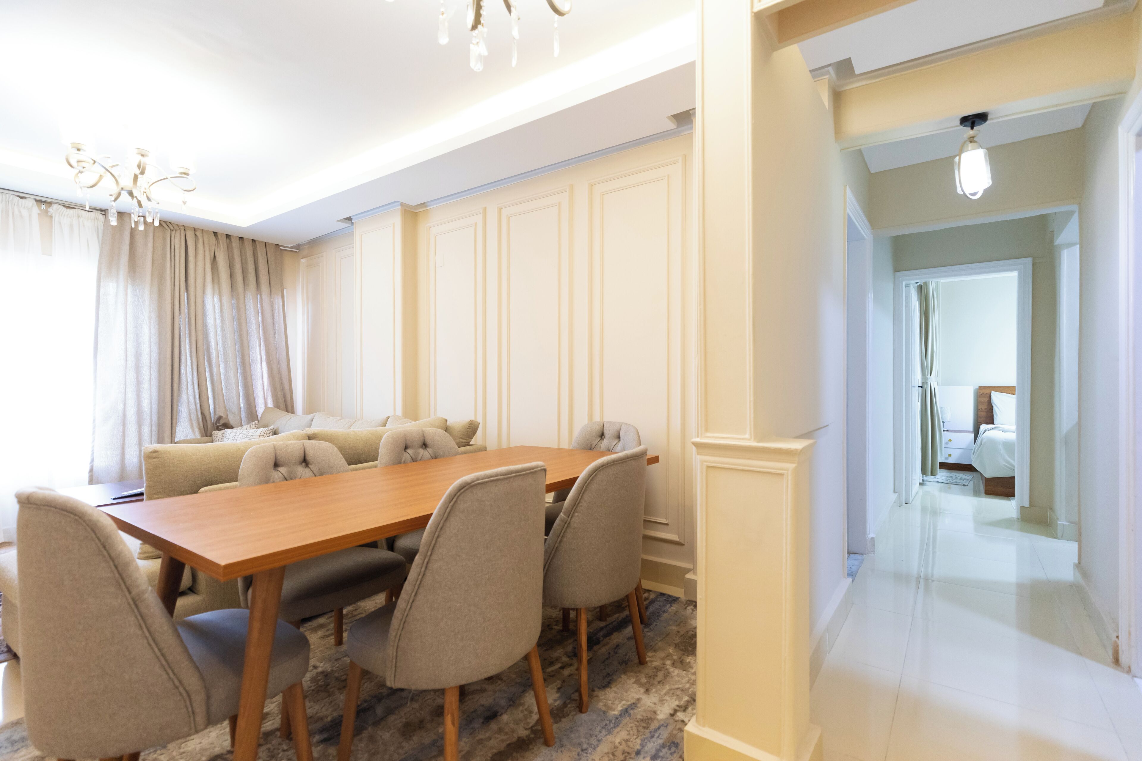A dining area with a wooden table and six chairs, a sofa, and a chandelier.