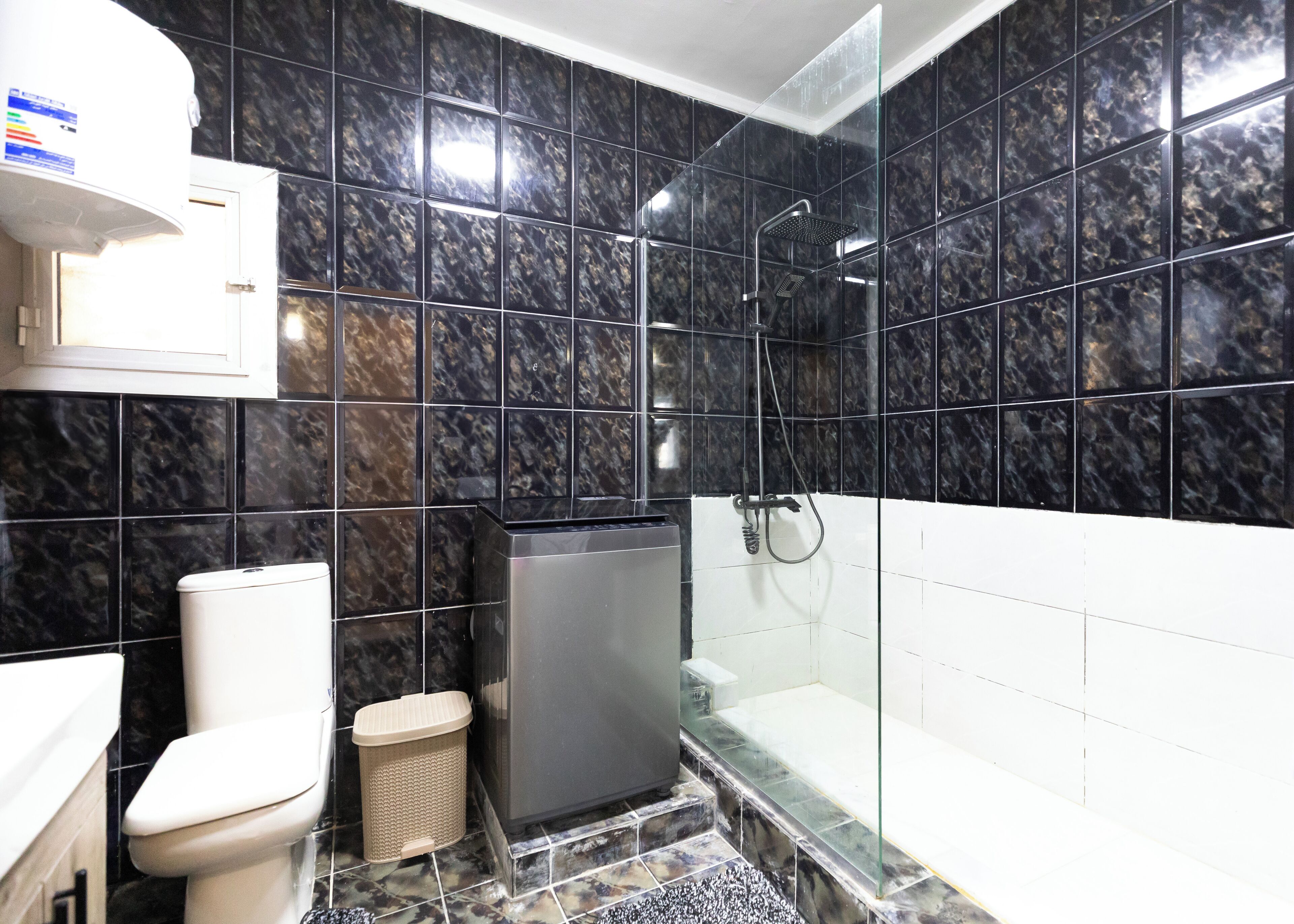 Une salle de bain avec des carreaux de marbre noir, des toilettes, une poubelle et une douche séparée par une paroi de verre.