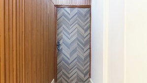 A hallway with wooden paneling on one side, a chevron-patterned door, and recessed ceiling lights. - 2BRs CityStar Mall Apartment (Al Golf, Nasr City)