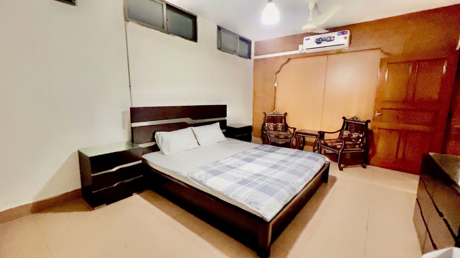 Ein Schlafzimmer mit einem Bett, Nachttischen, einem Schreibtisch, einem Stuhl, einem Kleiderschrank und einem Deckenventilator.