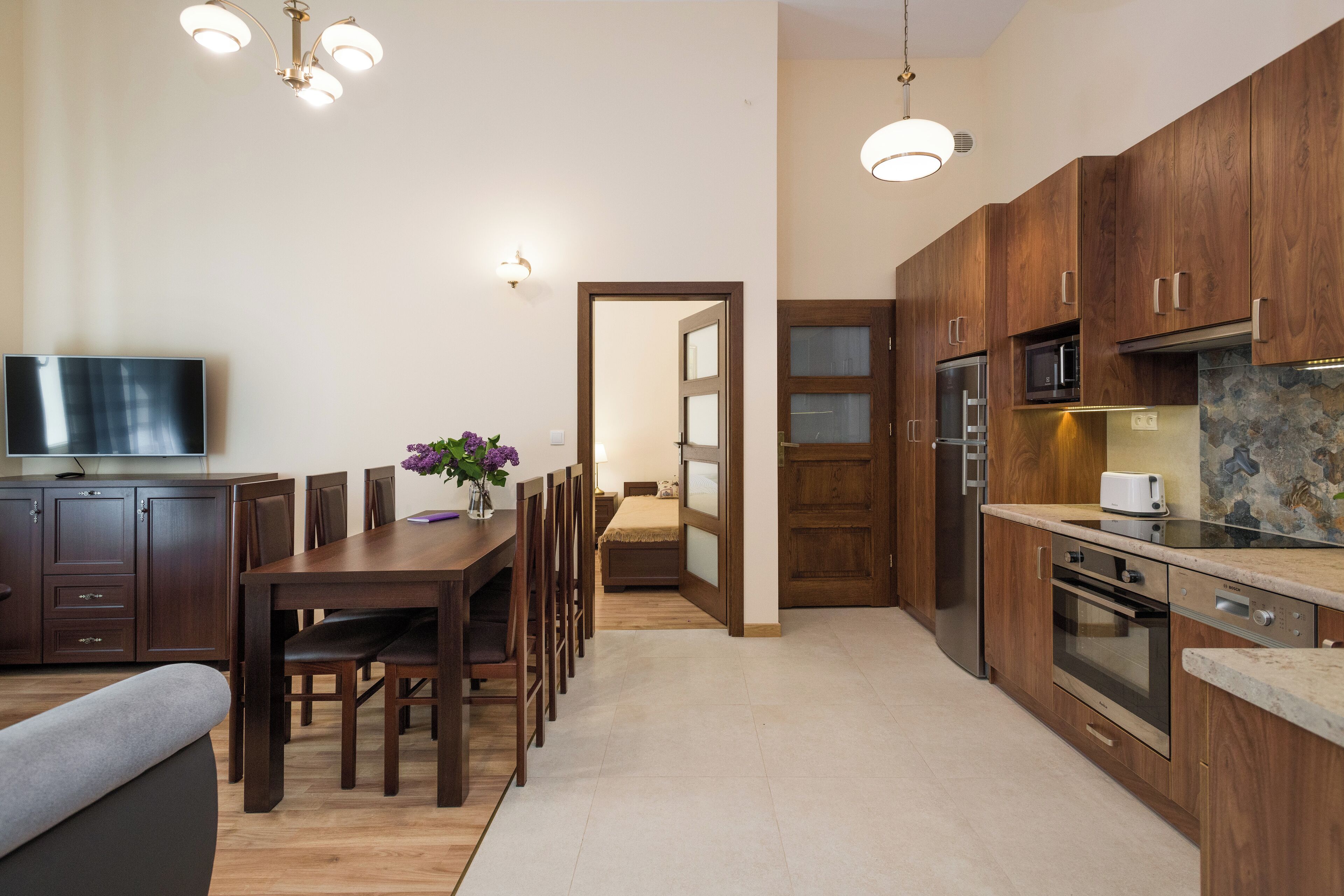 Een moderne keuken met houten kastjes, een eethoek met een tafel en stoelen, en een televisie aan de linkerkant.