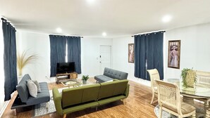 A spacious living room with a green sofa, a grey sofa, a dining table with chairs, and a flat-screen TV. - Spacious delray suite (Delray Beach)