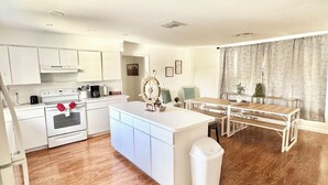 A modern kitchen with white cabinets, a central island, and a dining area with a table and benches. - Spacious delray suite (Delray Beach)