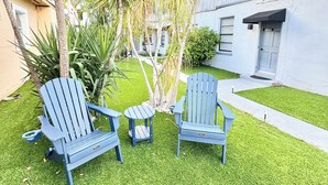 A backyard with two blue Adirondack chairs, a small round table, and a lawn. - Spacious delray suite (Delray Beach)